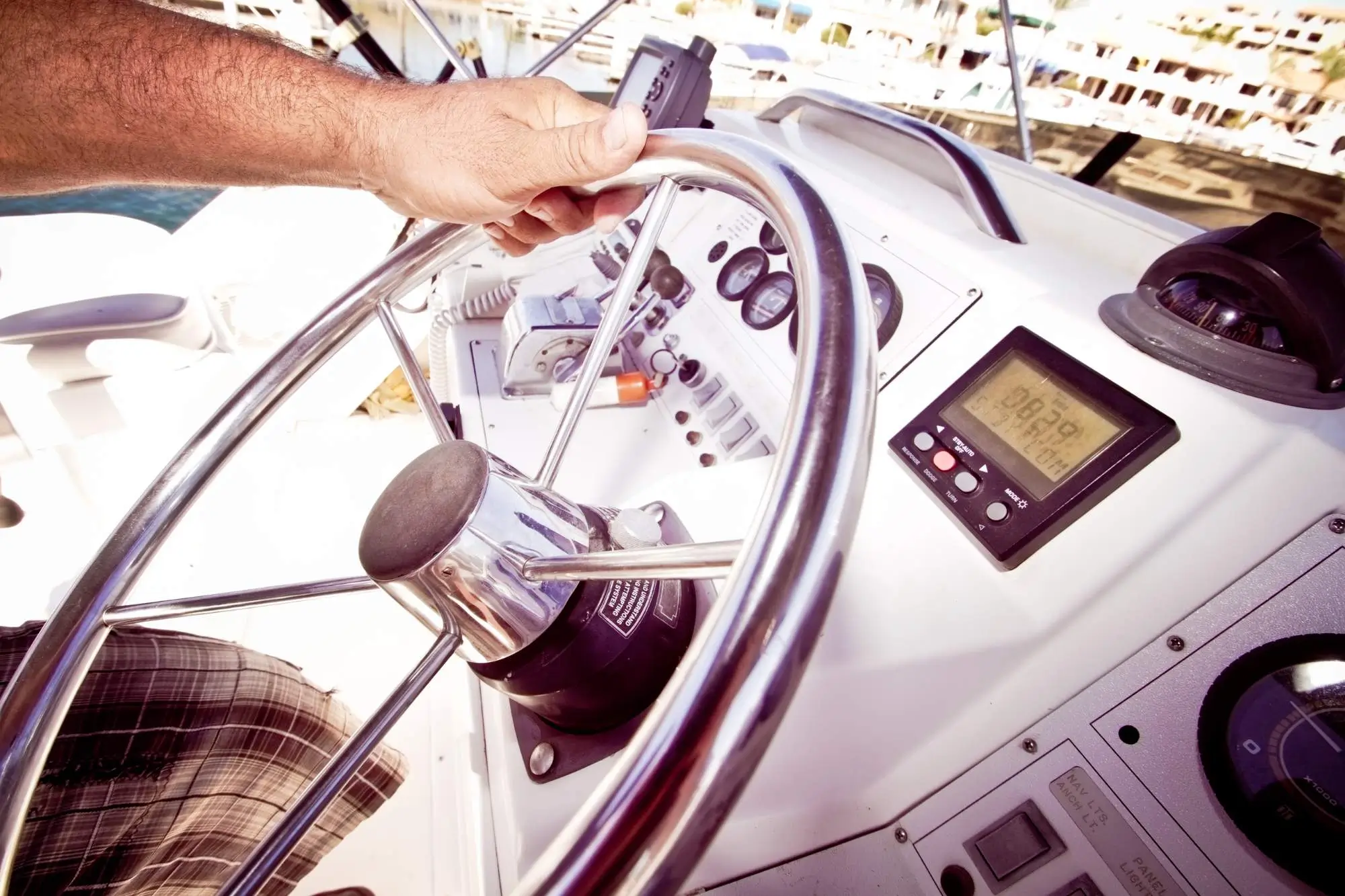 Person’s hand steering a boat with a stainless-steel wheel beside navigation instruments and gauges.