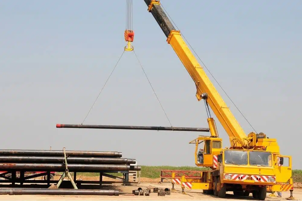 Slewing mobile crane lifting steel pipe with hook and slings, open outdoor training yard